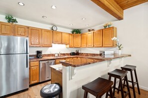 A modern kitchen with wooden cabinets, stainless steel appliances, a granite countertop, and a bar area with stools. - Riverside Dream | Short Walk to Main Street & Hike (Telluride)