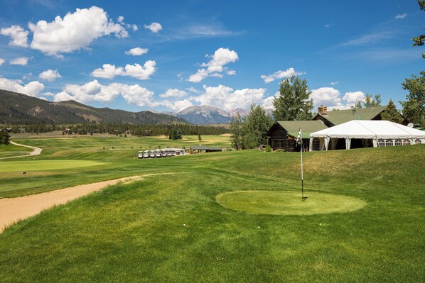 A golf course with a tent, a building, and mountains in the background.