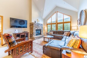 A spacious living room with a stone fireplace, leather furniture, and large windows offering a view of the outdoors.
