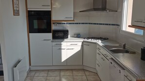 A modern kitchen with white cabinets, a built-in oven, a microwave, a gas stove, and a sink. - Maison de Vacances Moguériec (Sibiril)
