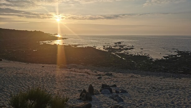 A beach with rocks and sand, and the sun setting in the background. - Maison de Vacances Moguériec (Sibiril)