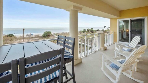 A balcony with a table and chairs, overlooking a beach and ocean.