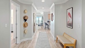 A hallway with a bench, a rug, and a wall with hats. There is a door on the left and a kitchen area in the background.
