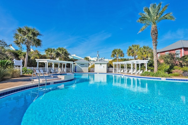 A clear blue pool with lounge chairs and palm trees.