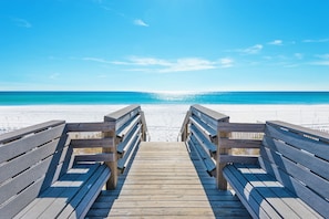 A wooden boardwalk leading to a beach with a clear blue sky.