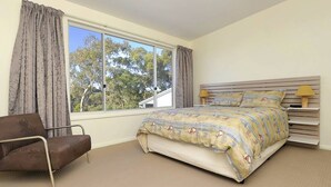 Una camera da letto con un letto, una sedia, una finestra con tende e un comodino con lampade.