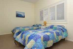 A bedroom with two beds, a nightstand, a lamp, a window with blinds, and a painting on the wall.