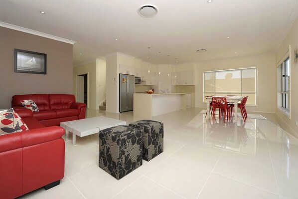 A modern living room with a red sofa, a white coffee table, and a patterned ottoman.