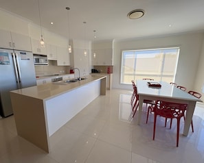 A modern kitchen with a central island, stainless steel appliances, pendant lighting, and a dining area with red chairs.
