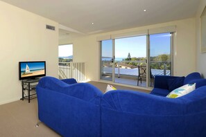 A living room with a large TV, blue sofas, and a balcony with a view.