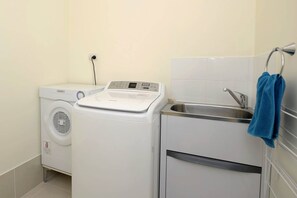 A laundry area with a washing machine, a dryer, and a sink with a towel hanging on the wall.