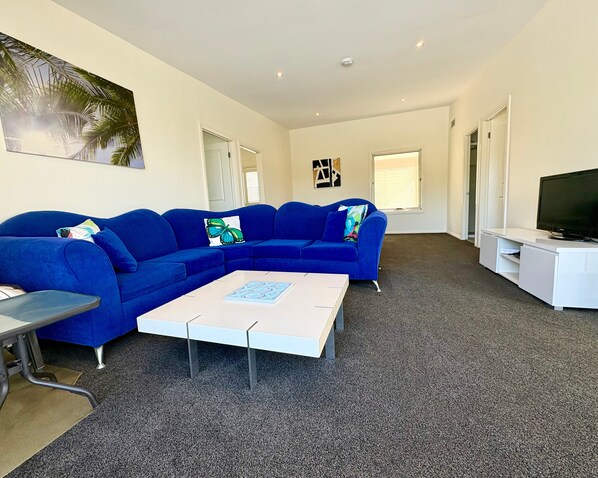 A modern living room with a blue sectional sofa, a coffee table, a flat-screen TV, and a painting on the wall.