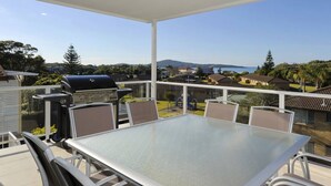 Una veranda riparata all'aperto con tavolo e sedie, con vista su una zona residenziale con case e un tratto d'acqua.