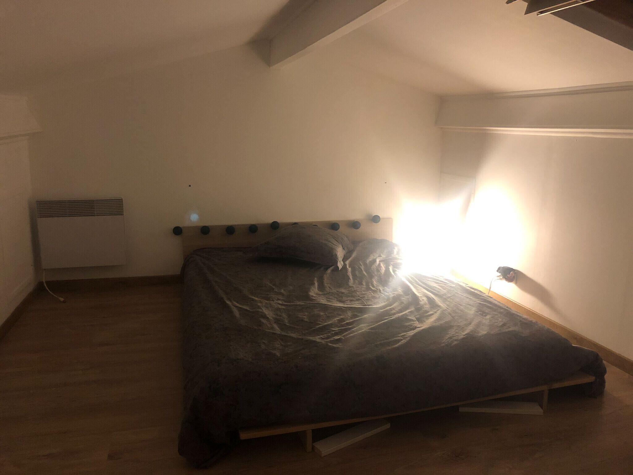 A single bed in a room with a sloped ceiling and a radiator on the wall.