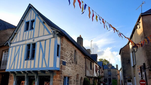 A narrow cobblestone street lined with traditional half-timbered houses, a sign indicating a commercial area, and a clear sky. - Apartment (Guérande)