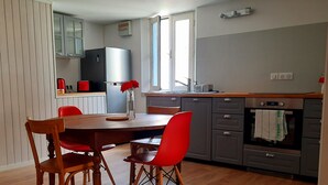 A modern kitchen with wooden cabinets, a stainless steel refrigerator, and a dining table with red chairs. - Apartment (Guérande)