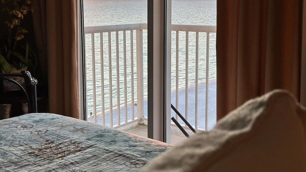 Una stanza con un letto, vista sul mare da un balcone e una pianta a sinistra.