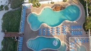 Una vista aerea di un resort con due piscine comunicanti, zone relax e palme.