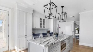 A kitchen with white cabinets, a marble island, and pendant lights.