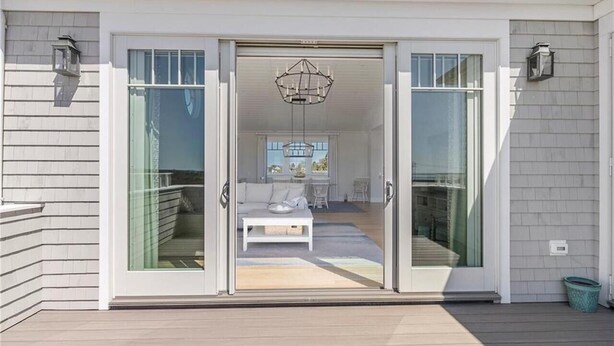 A modern house with a sliding glass door leading to a living area with a white sofa, a coffee table, and a chandelier.