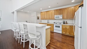 Eine moderne Küche mit Holzausstattung, einem weißen Kühlschrank und einer Bar mit weißen Hockern.