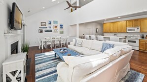 Ein modernes Wohnzimmer mit einem weißen Sofa, einem Esstisch und einer Küchenzeile mit Holzschränken und einer Mikrowelle.