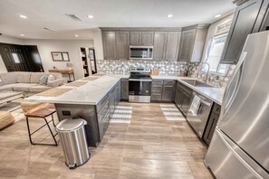 A modern kitchen with grey cabinets, stainless steel appliances, and a large island.