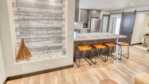 Een moderne keuken met een centraal eiland, barstoelen en een decoratief wandpaneel.