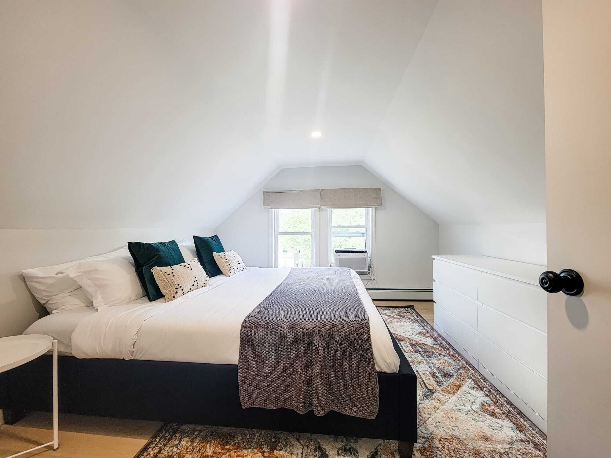 Une chambre à coucher avec un lit, des oreillers, une table de chevet, une fenêtre et un radiateur.