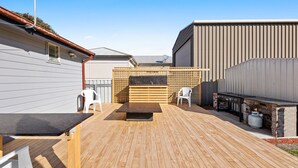 Eine Holzterrasse mit Grill, zwei weißen Plastikstühlen und einem Holztisch.
