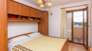 A bedroom with a bed, wooden wardrobe, and a balcony with a view. - Apartment Jele (Zupa dubrovacka)