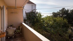 A balcony with a table and chairs, a view of trees, and a building in the background. - Apartment Jele (Zupa dubrovacka)