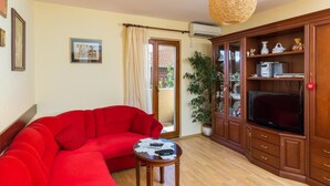 A living room with a red sofa, a wooden cabinet with a TV, and a hanging light fixture. - Apartment Jele (Zupa dubrovacka)