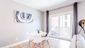 Ein modernes Wohnzimmer mit einem runden weißen Tisch und zwei Stühlen, einem grauen Sofa und zwei abstrakten Bildern an der Wand.