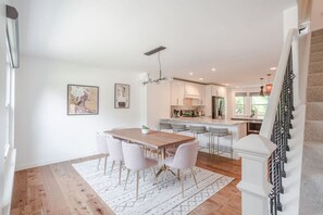 Una cocina moderna con armarios blancos, una mesa de comedor de madera y taburetes de bar.