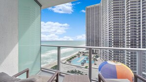 A balcony with wicker furniture, a view of the ocean, and a pool area with a beach and palm trees. - Ocean front 2 bed 15th floor Hollywood Miami (Hollywood)