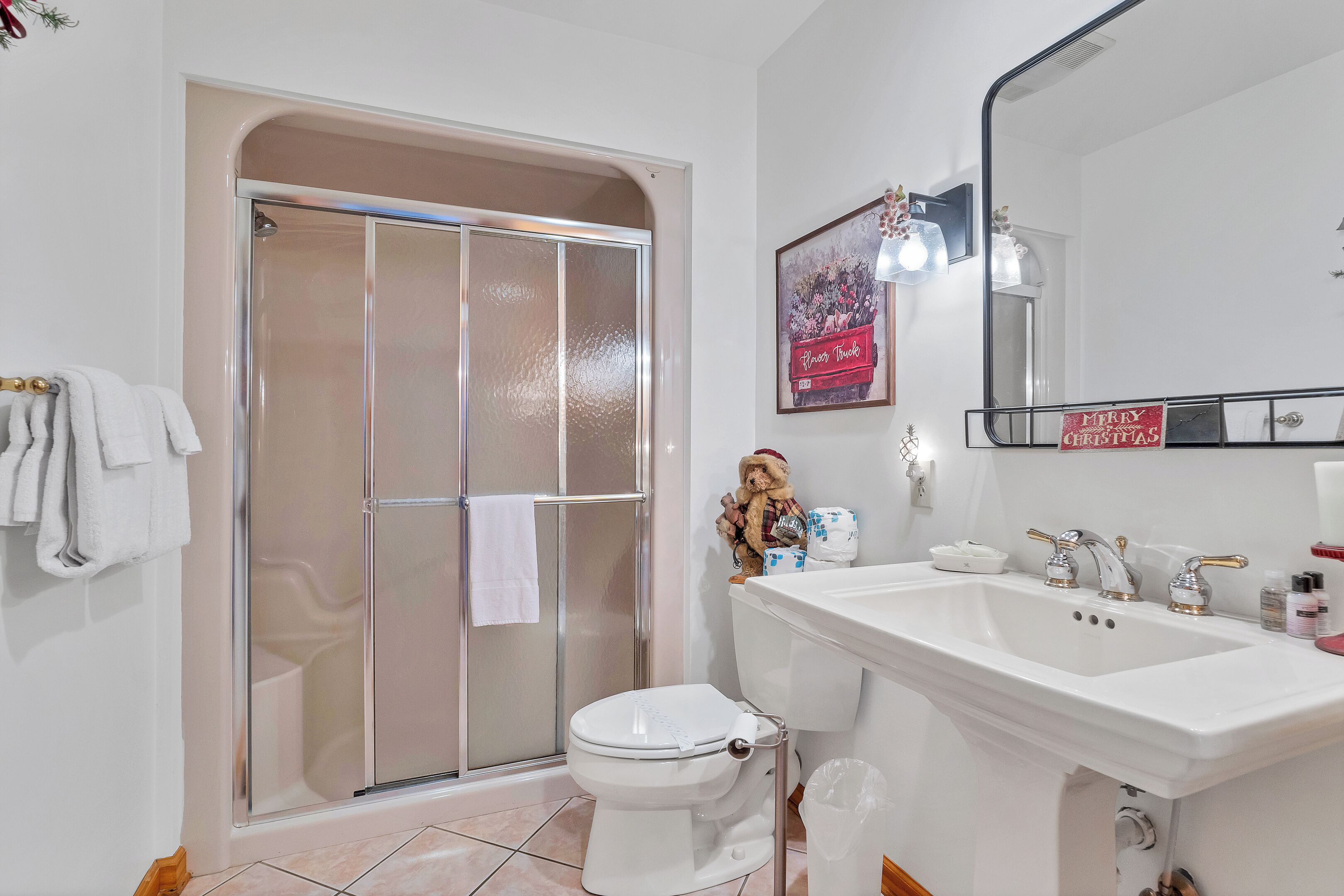 Un bany amb plat de dutxa de vidre, un vàter blanc i un gran lavabo amb un mirall a sobre.