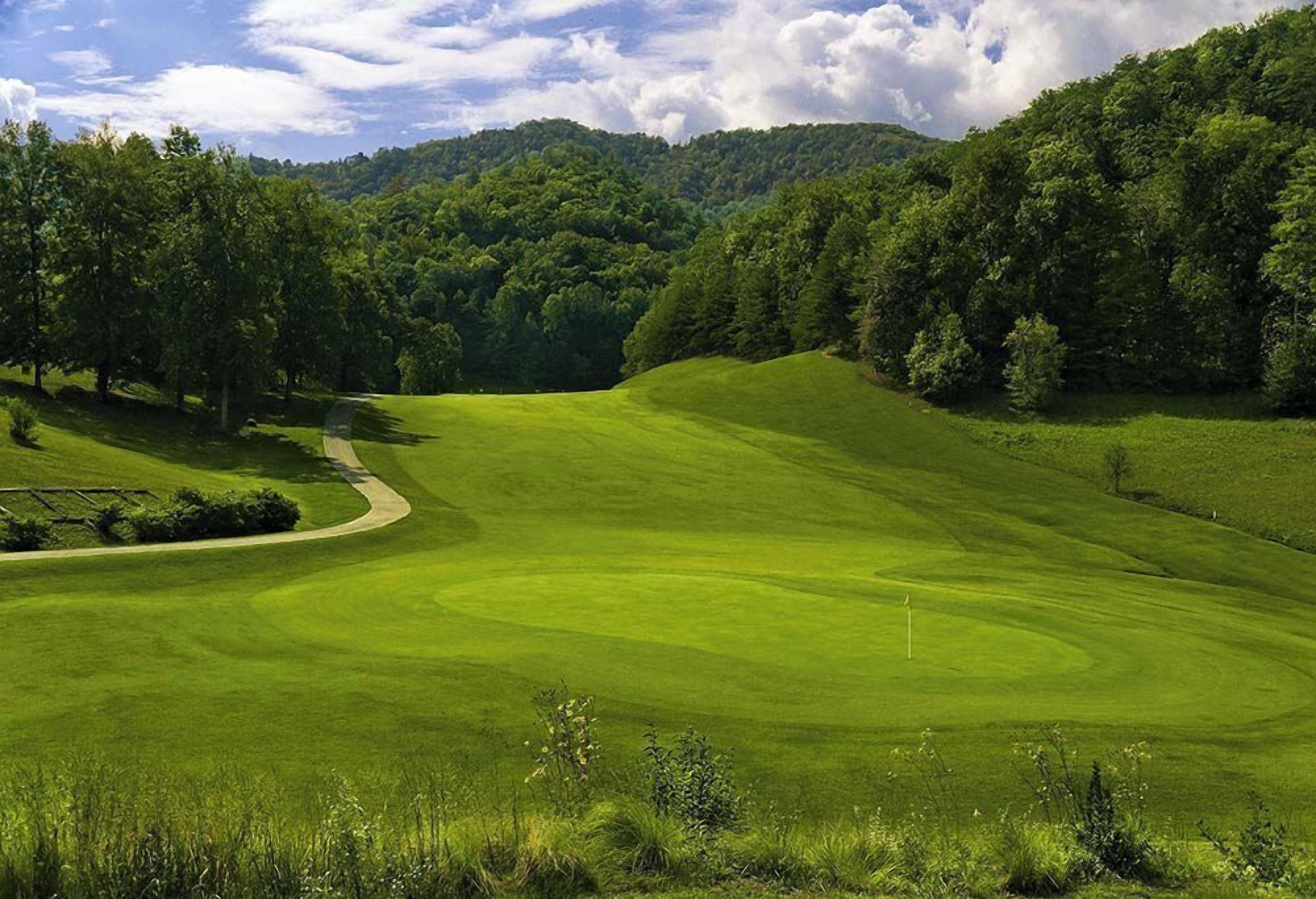 A golf course with rolling hills, trees, and a clear sky.