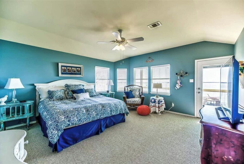 A bedroom with a bed, a chair, a small table, a lamp, and a ceiling fan.