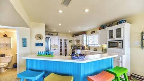 A kitchen with a central island, stools, cabinets, and a microwave.