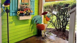 A vibrant green exterior with a 'Welcome' sign, a window with blue shutters, and a bird sculpture.