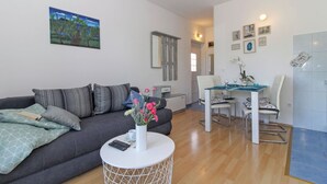 En moderne stue med en grå sofa, et rundt sofabord og et spiseområde med et hvidt bord og stole.