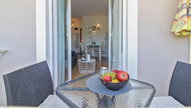 En balkon med et bord, en skål med frugt, en stol og udsigt til en opholdsstue med en sofa og sofabord.
