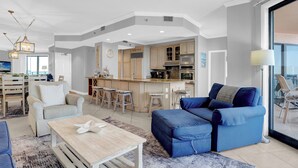 A spacious living area with a sofa, coffee table, and a kitchen in the background. - SeaChase 1002W BY Liquid Life (Orange Beach)