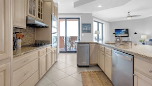 A modern kitchen with granite countertops, stainless steel appliances, and light wood cabinetry. - SeaChase 1002W BY Liquid Life (Orange Beach)