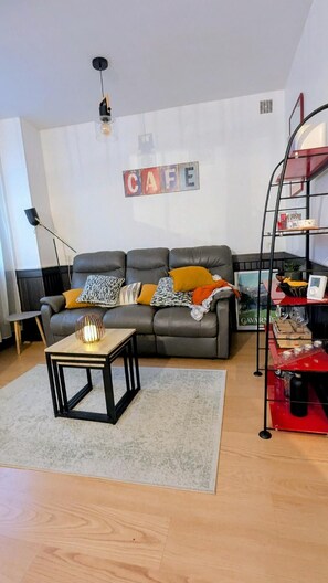 Een woonkamer met een grijze bank, een klein houten bijzettafeltje en een rode metalen boekenkast.