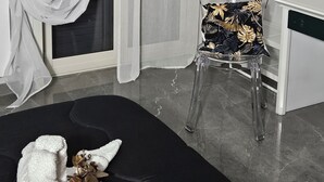 A modern room with a black sofa, a clear chair with a patterned cushion, a white desk, and a large mirror on the wall. - La Punta (San Giovanni la Punta)