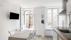 A modern kitchen with a dining area, a TV mounted on the wall, and a view of the outside. - Le Coco de Cancale - Duplex proche mer (Cancale)