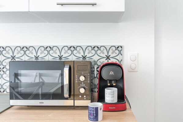 Una cocina con microondas, cafetera y una taza sobre la encimera.