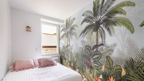 A bedroom with a large window, a bed with pink pillows, and a tropical-themed mural on the wall. - Le Coco de Cancale - Duplex proche mer (Cancale)